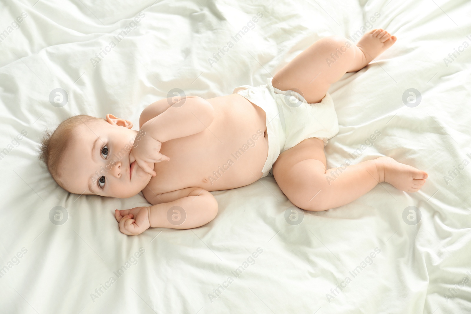 Photo of Cute little baby in diaper lying on bed, above view