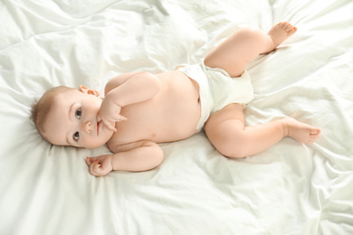 Photo of Cute little baby in diaper lying on bed, above view