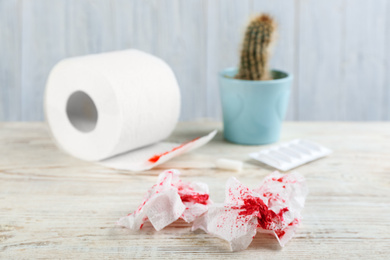 Photo of Sheets of toilet paper with blood on white wooden table. Hemorrhoid problems