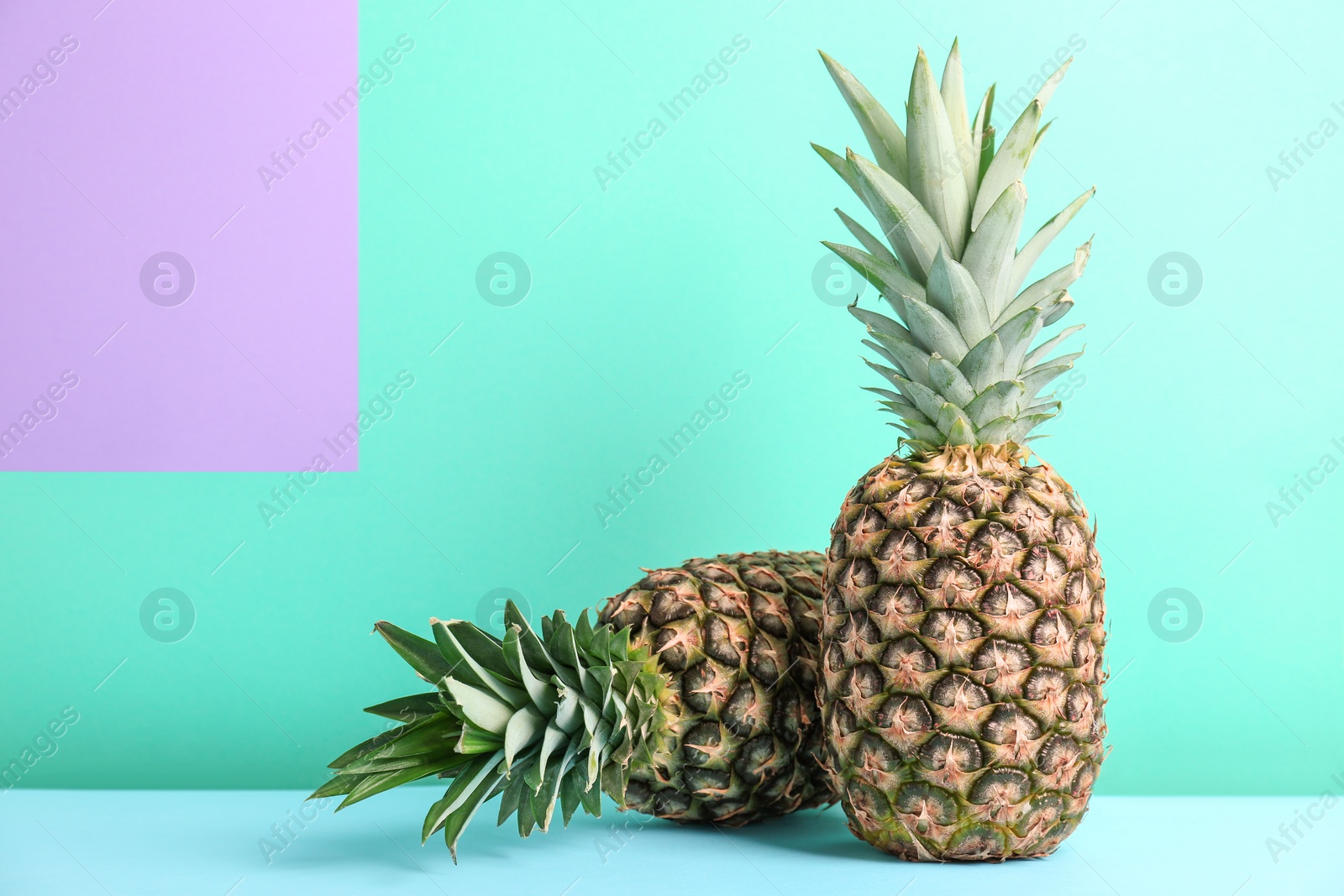 Photo of Fresh pineapples on table against color wall