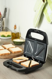 Photo of Modern sandwich maker with bread slices on wooden table