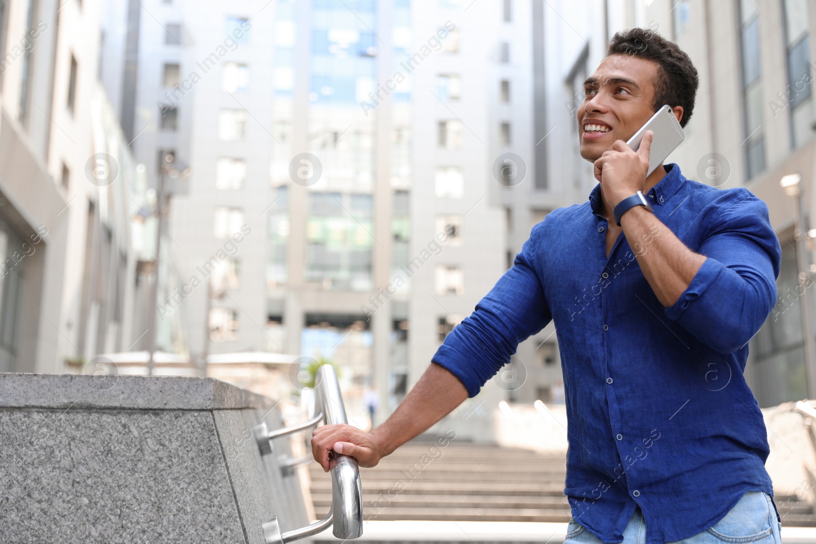 Photo of Handsome young African-American man talking on mobile phone outdoors. Space for text