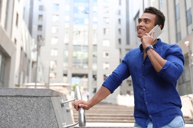 Handsome young African-American man talking on mobile phone outdoors. Space for text