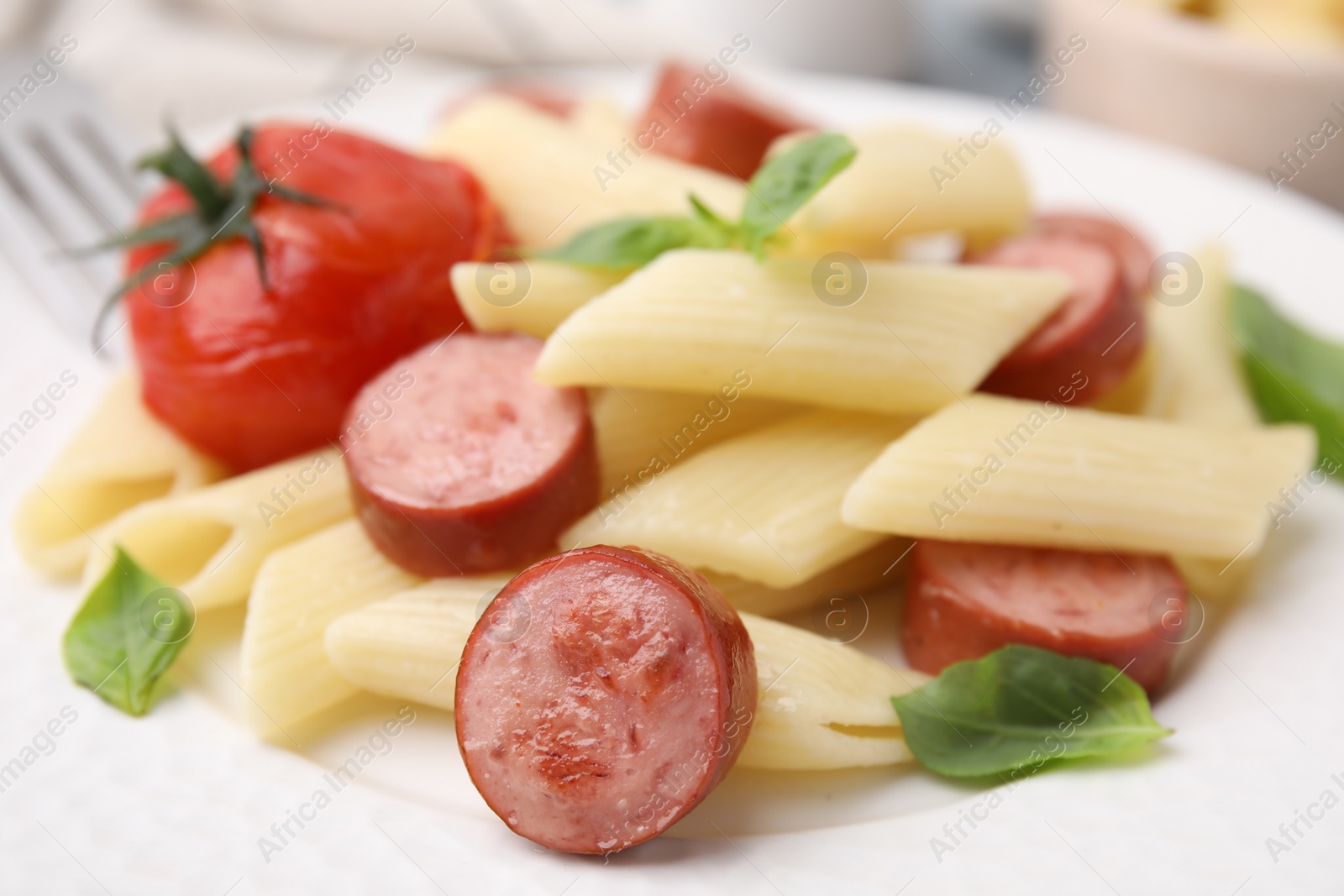 Photo of Tasty pasta with smoked sausage, tomato and basil on plate, closeup