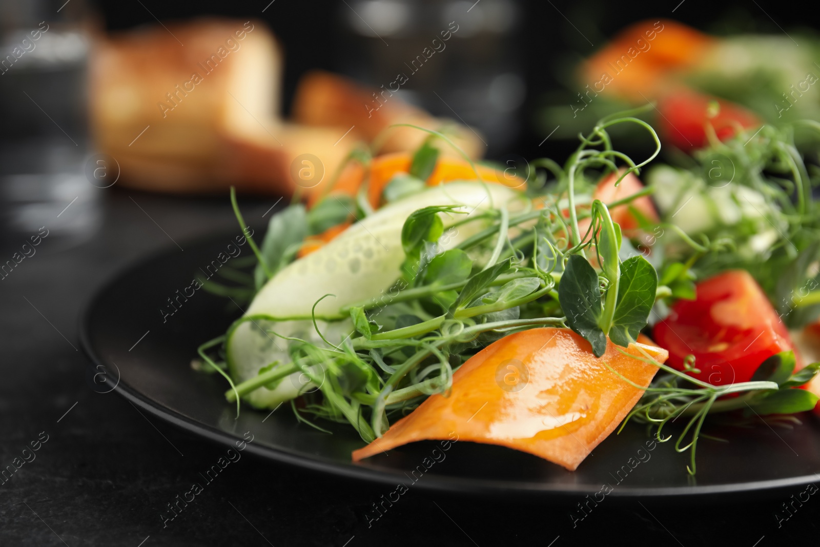 Photo of Delicious vegetable salad with microgreen on black table, closeup