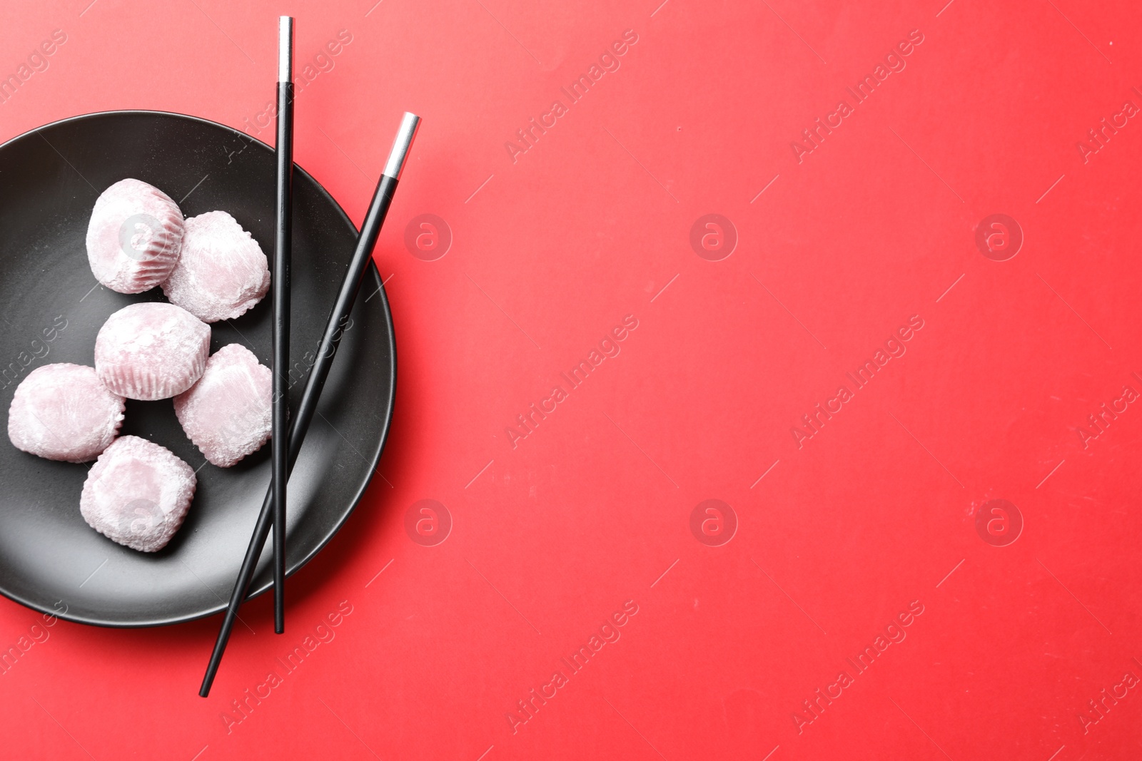 Photo of Black plate with delicious mochi and chopsticks on red background., top view. Space for text