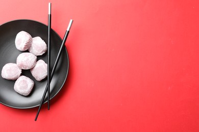 Black plate with delicious mochi and chopsticks on red background., top view. Space for text