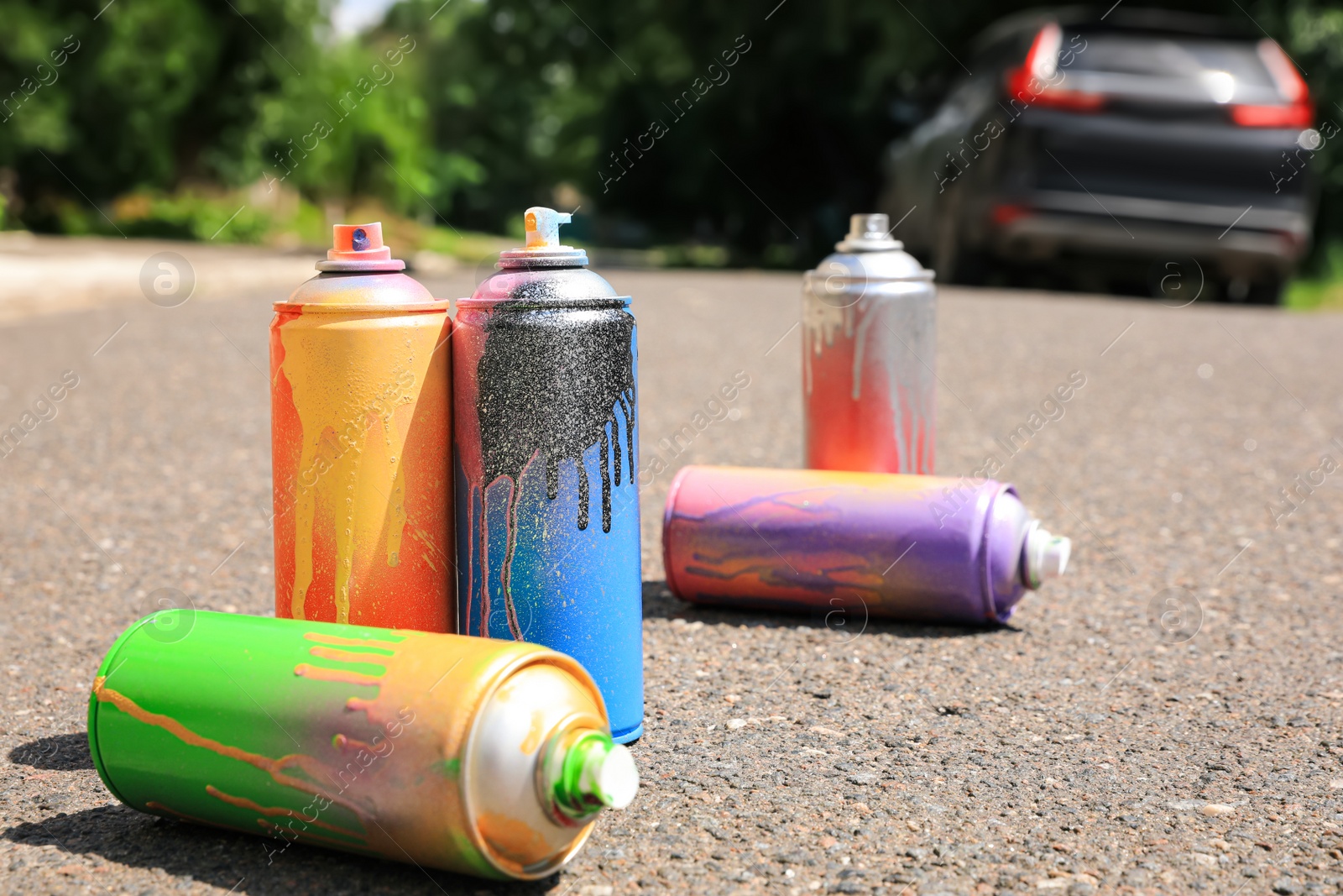 Photo of Used cans of spray paint on asphalt road. Graffiti supplies