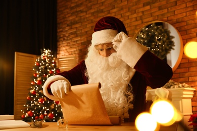 Santa Claus reading wish list at table indoors