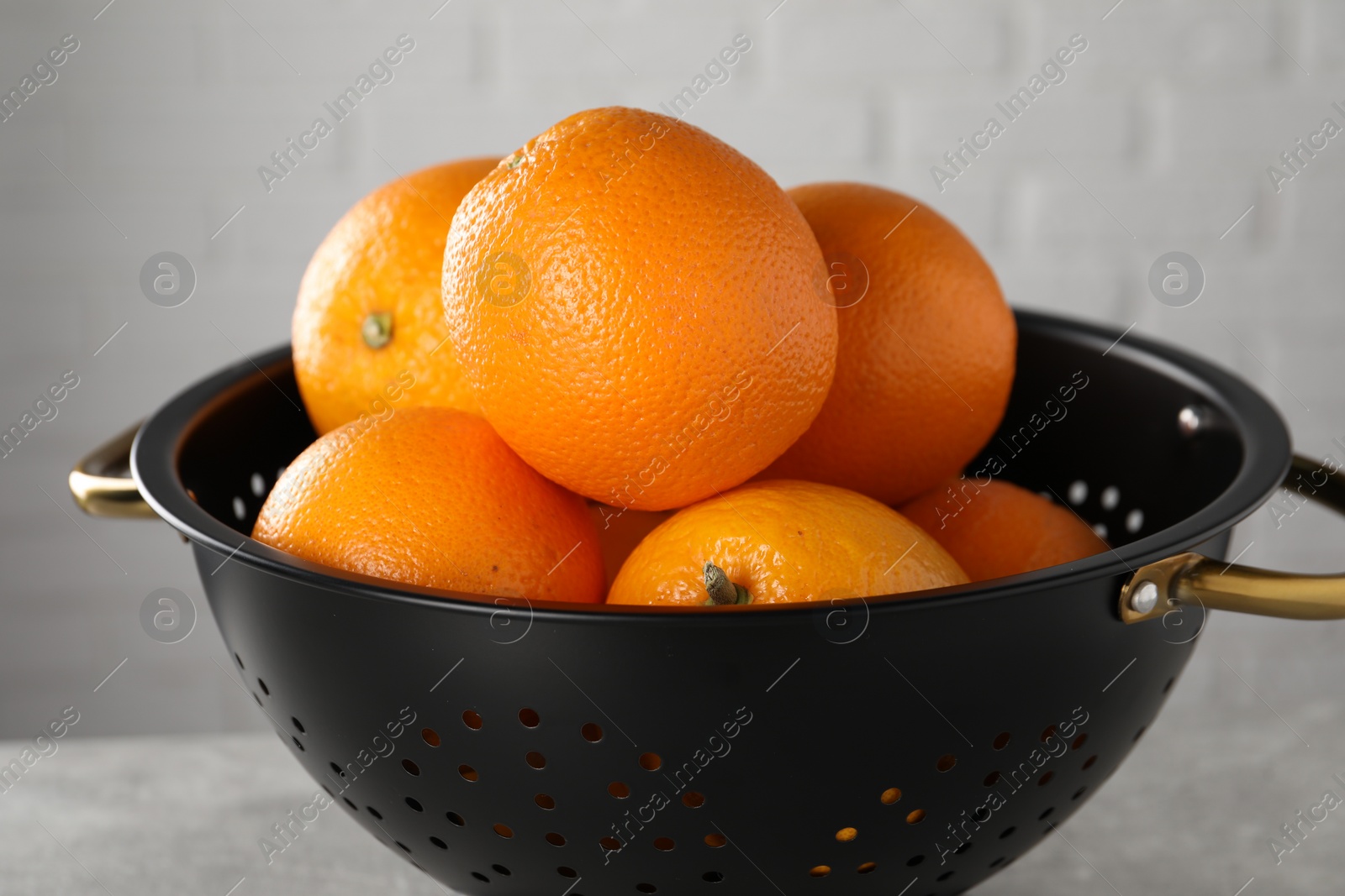 Photo of Fresh ripe oranges in black colander on light background, closeup