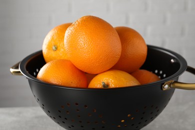 Photo of Fresh ripe oranges in black colander on light background, closeup