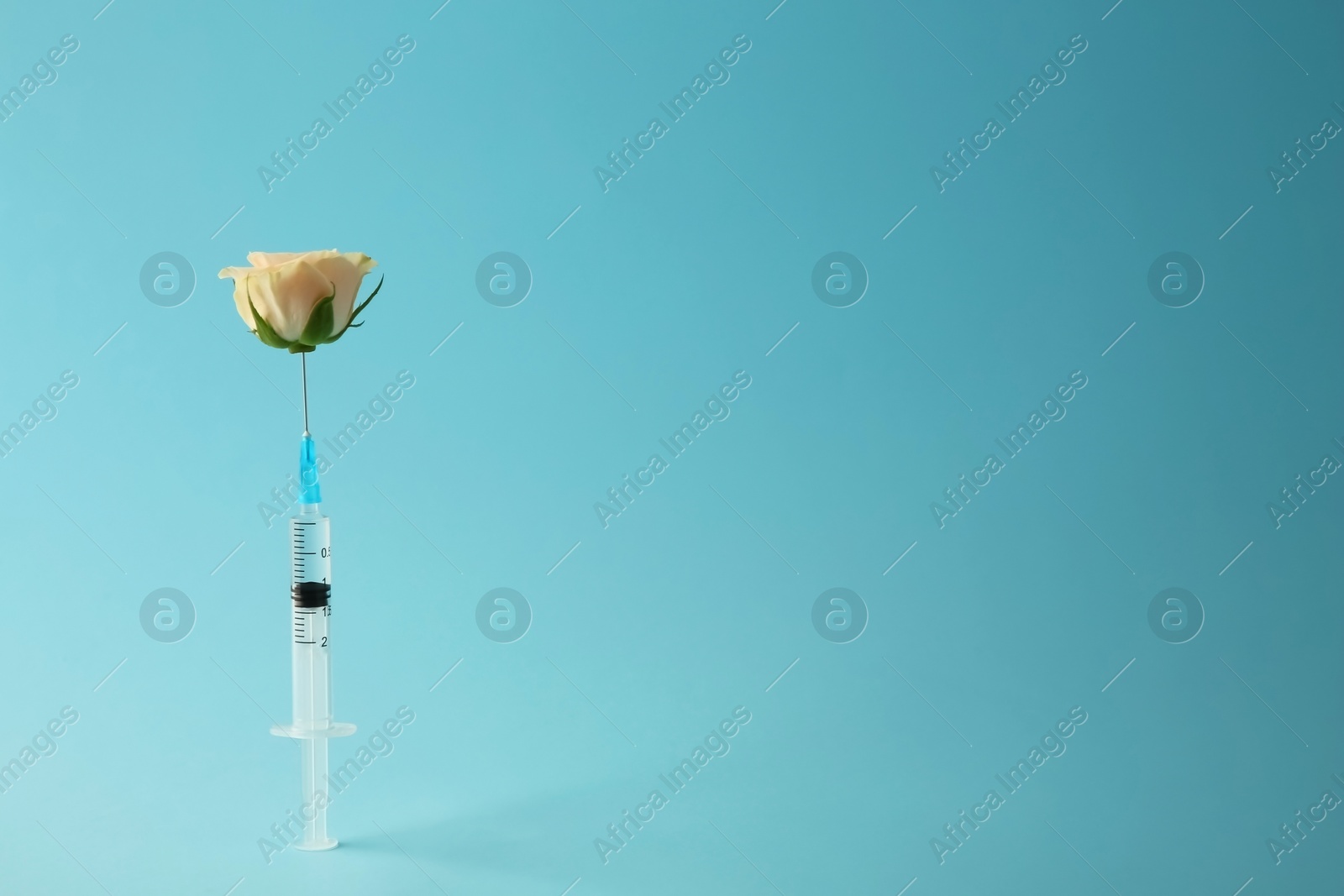 Photo of Medical syringe and beautiful rose on light blue background, space for text