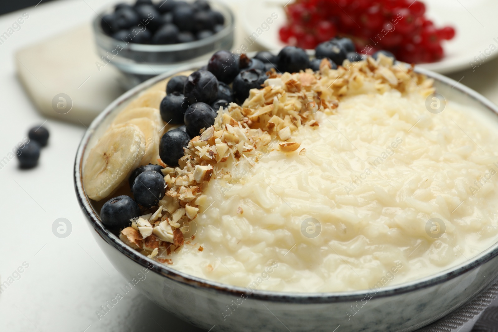 Photo of Delicious rice pudding with banana, blueberries and almond on light table, closeup