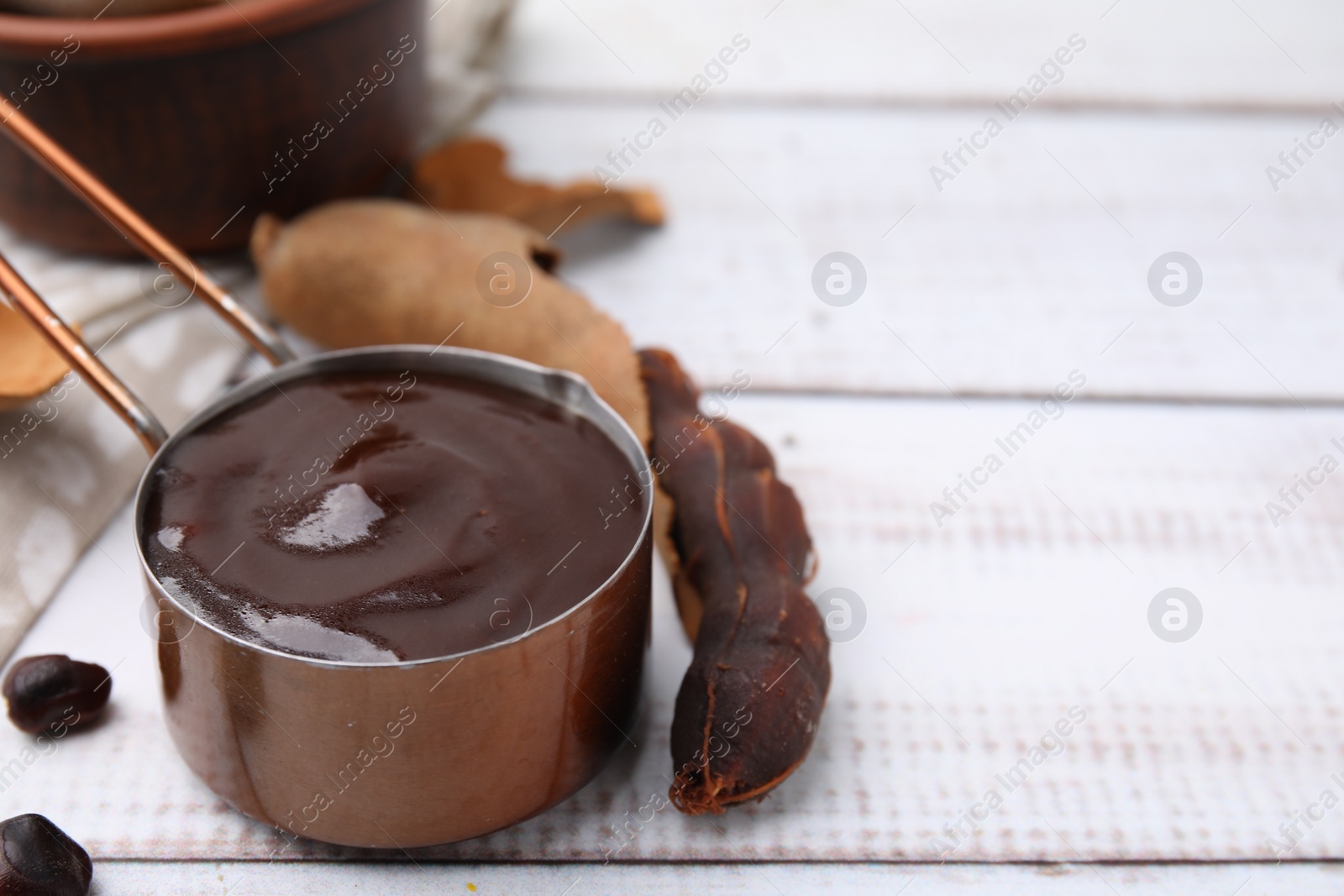 Measuring cup with tasty tamarind sauce and fresh pods on white wooden table. Space for text Photo of Measuring cup with tasty tamarind sauce and fresh pods on white wooden table. Space for text