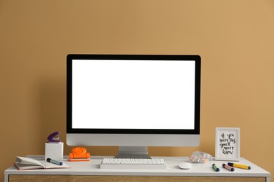 Photo of Stylish workplace with computer and stationery on wooden table near beige wall