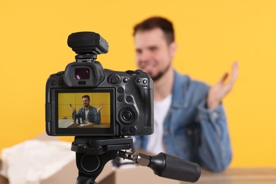 Photo of Fashion blogger showing sneakers while recording video at table against orange background, focus on camera