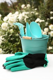 Photo of Gardening gloves and bucket with different tools on white wooden table outdoors
