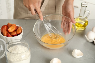 Photo of Woman whipping eggs at grey table, closeup. Cooking of delicious cake