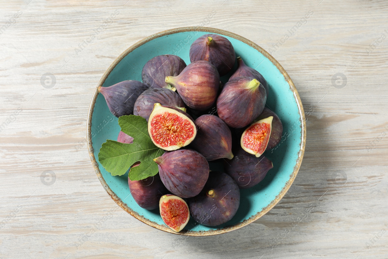 Photo of Plate with fresh ripe figs and green leaf on white wooden table, top view