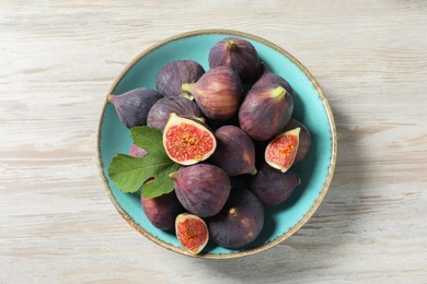 Plate with fresh ripe figs and green leaf on white wooden table, top view