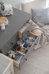 Modern open chest of drawers with clothes and accessories in baby room