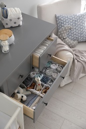 Photo of Modern open chest of drawers with clothes and accessories in baby room