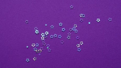 Photo of Many bright star shaped sequins on purple background, flat lay