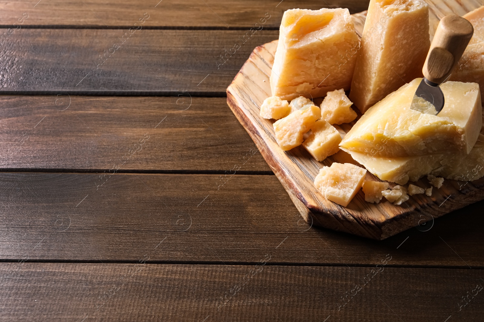 Photo of Pieces of delicious parmesan cheese with knife on wooden table. Space for text