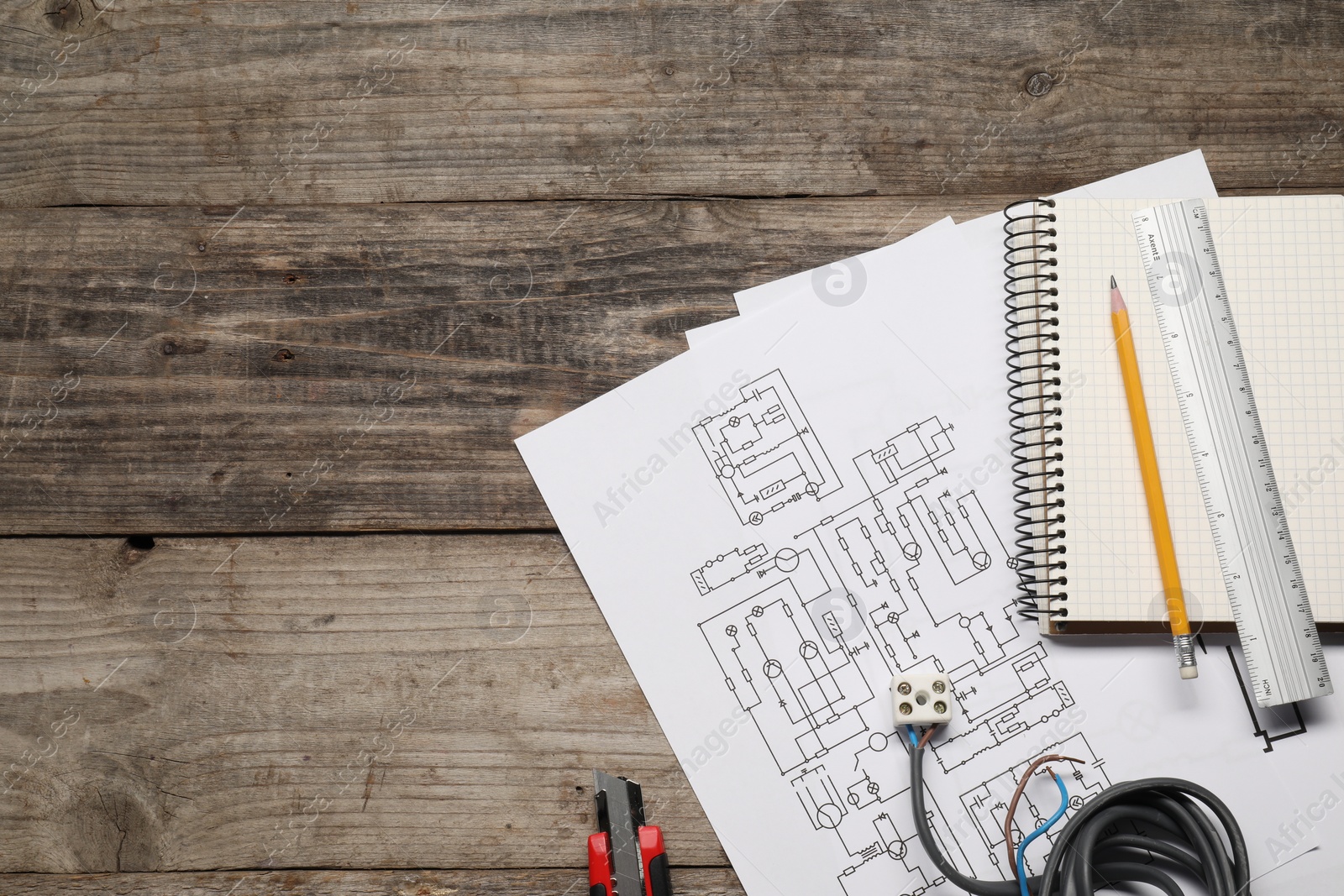 Photo of Wiring diagrams, wires, utility knife and office stationery on wooden table, flat lay. Space for text