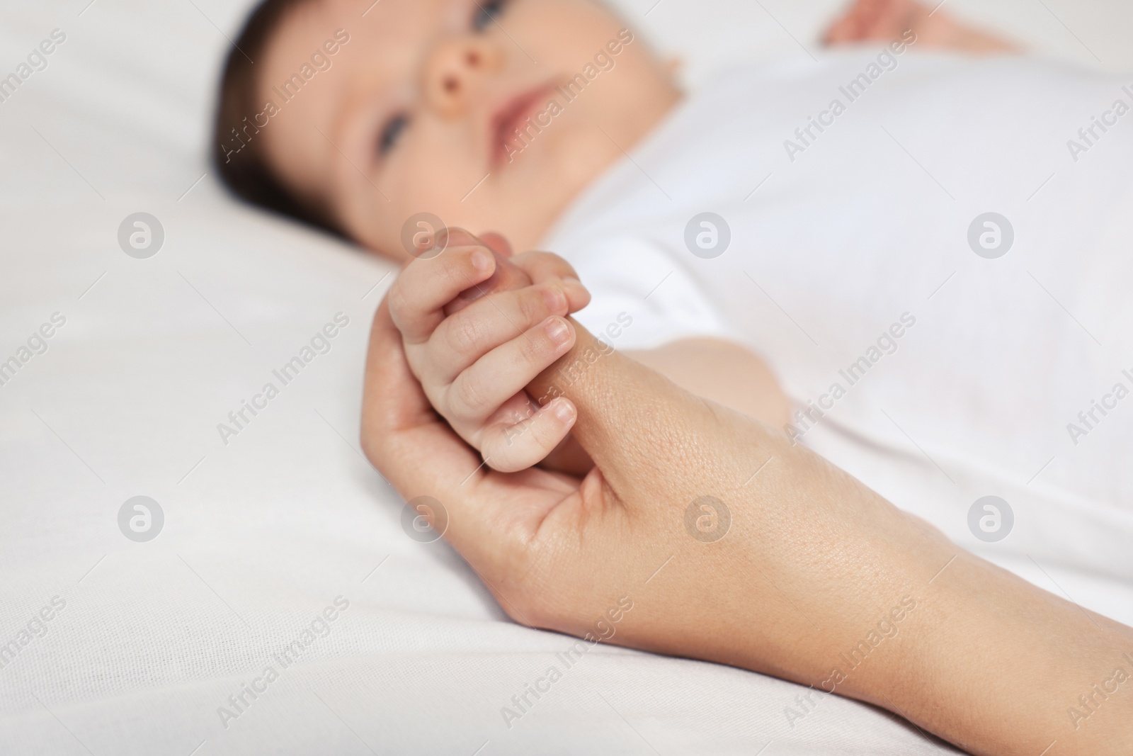 Photo of Mother holding hand of her little baby on bed, closeup