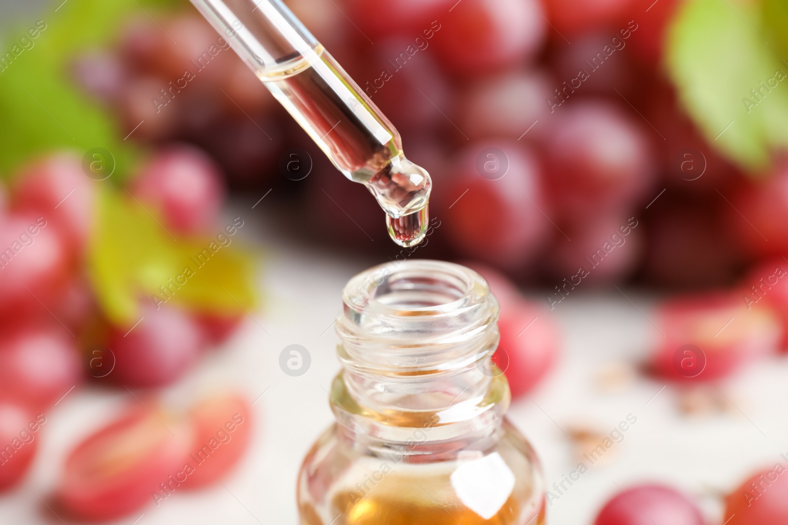 Photo of Natural grape seed oil dripping from pipette into bottle, closeup. Organic cosmetic