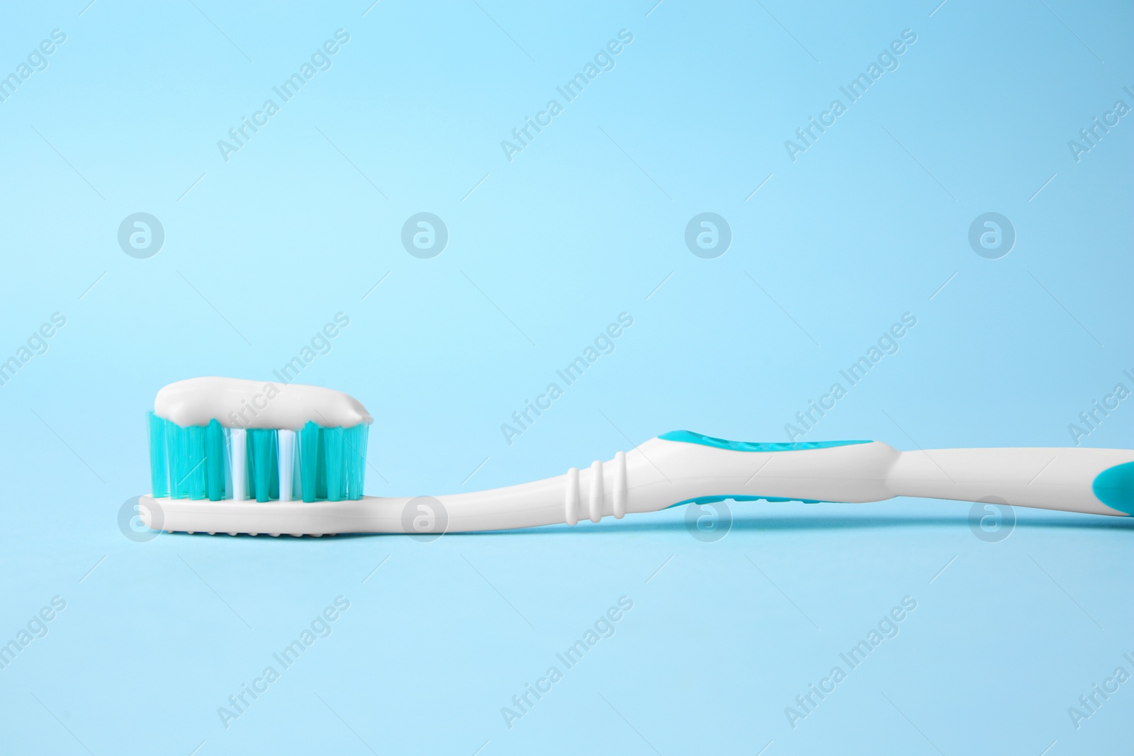 Photo of Brush with toothpaste on light blue background