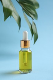 Bottle with cosmetic oil and green leaves on light blue background