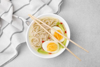 Photo of Bowl of delicious rice noodle soup with celery and egg on light grey table, flat lay