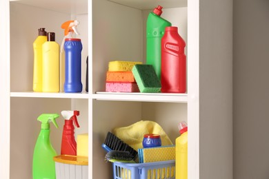 Photo of Shelving unit with detergents and cleaning tools near white wall indoors