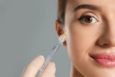 Photo of Beautiful woman getting facial injection on grey background, closeup. Cosmetic surgery