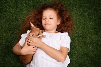 Photo of Cute little child with her Chihuahua dog on green grass, top view. Adorable pet