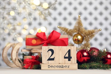 Photo of December 24 - Christmas Eve. Wooden block calendar and festive decor on white table against blurred lights