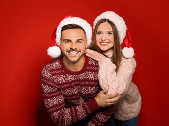 Photo of Couple wearing Christmas sweaters and Santa hats on red background