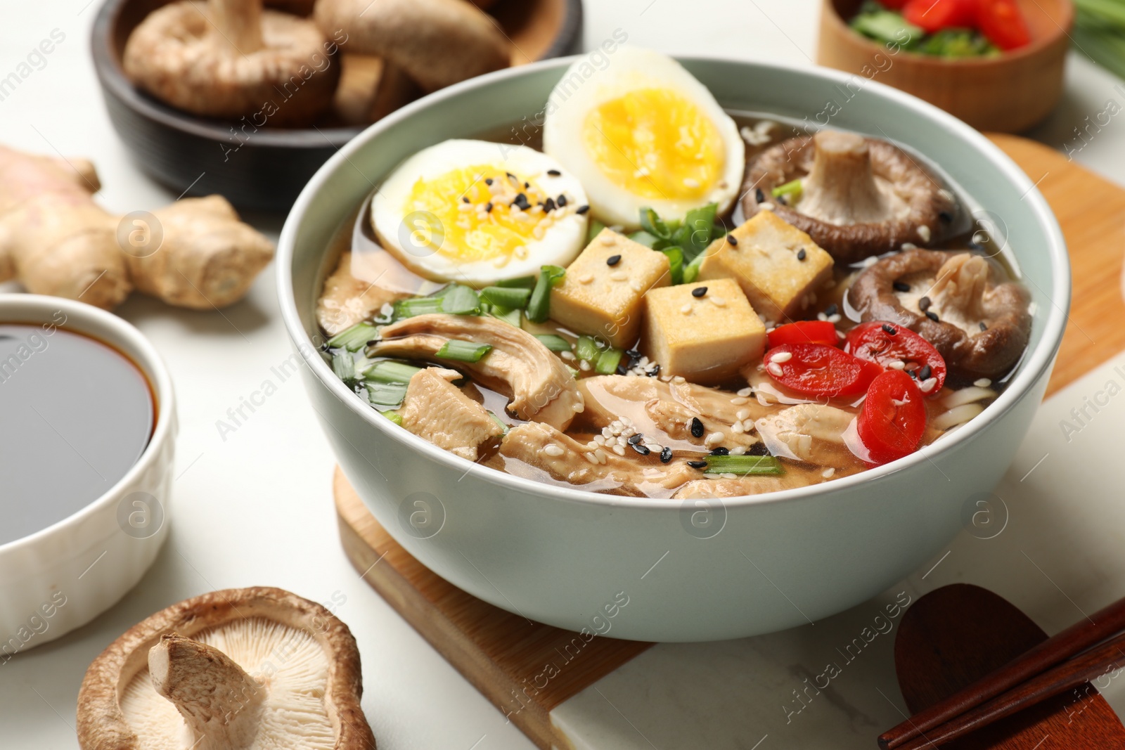 Photo of Bowl of delicious ramen and ingredients on white table, closeup. Noodle soup