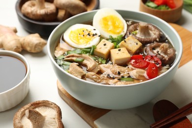 Photo of Bowl of delicious ramen and ingredients on white table, closeup. Noodle soup