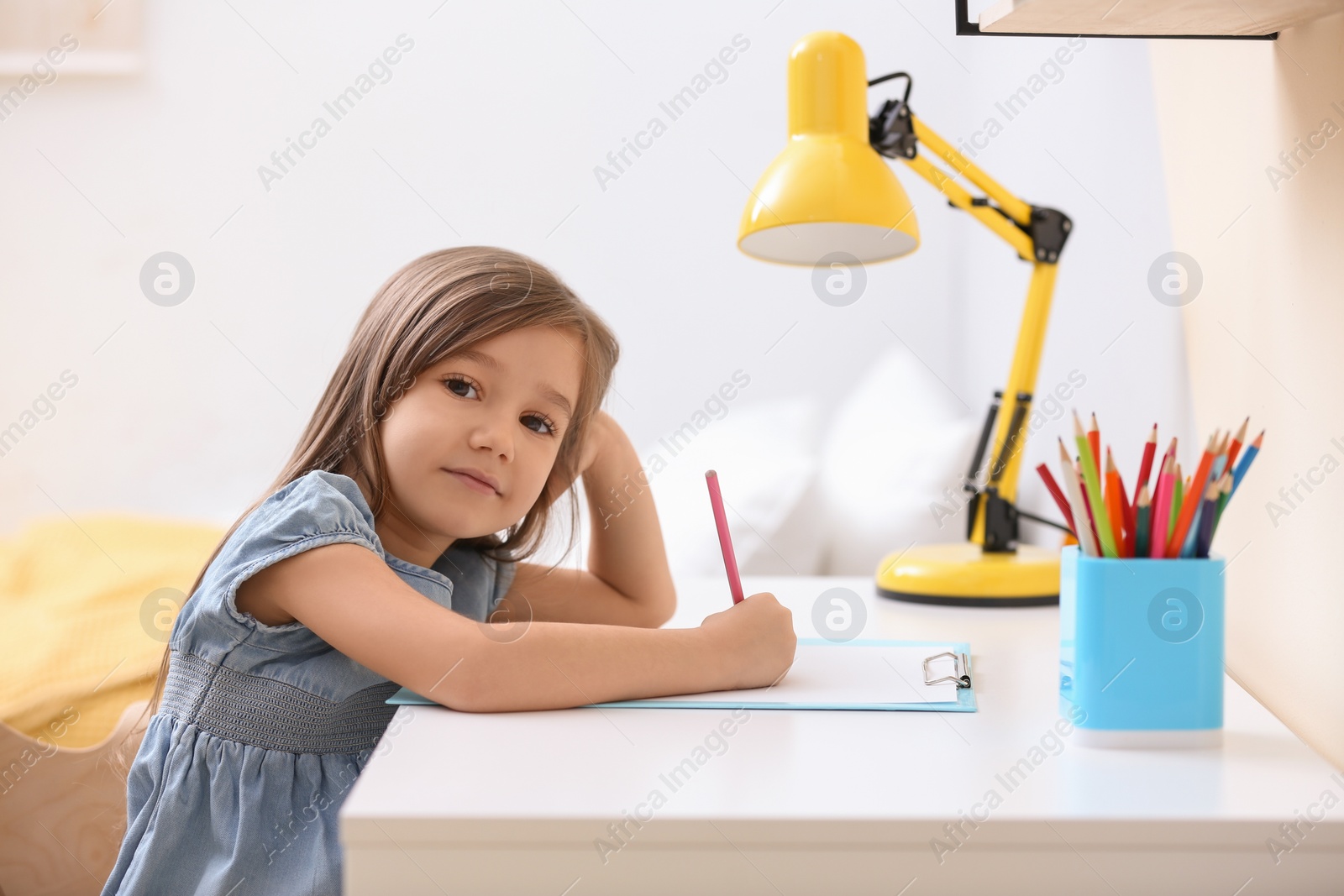 Photo of Cute little girl drawing at table in room