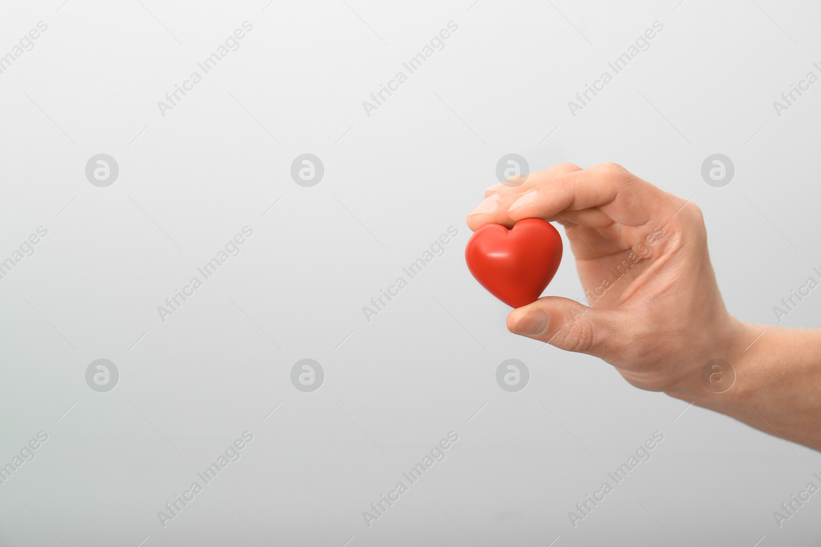 Photo of Man holding small red heart on light background. Heart attack concept