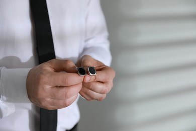 Man holding stylish cufflinks on blurred background, closeup. Space for text