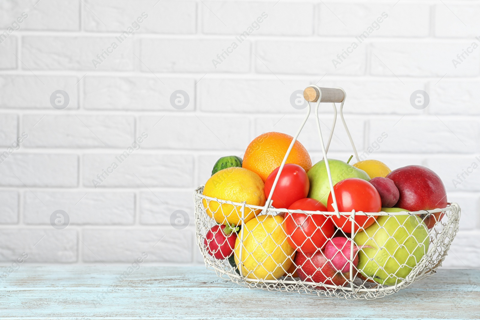 Photo of Basket with ripe fruits and vegetables on table against white brick wall. Space for text