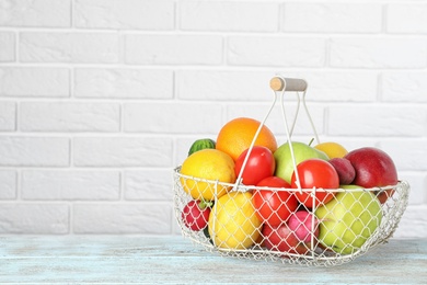 Photo of Basket with ripe fruits and vegetables on table against white brick wall. Space for text