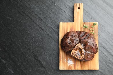 Piece of delicious grilled beef meat, thyme and salt on black table, top view. Space for text