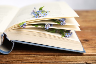 Beautiful forget-me-not flowers and book on wooden table, closeup