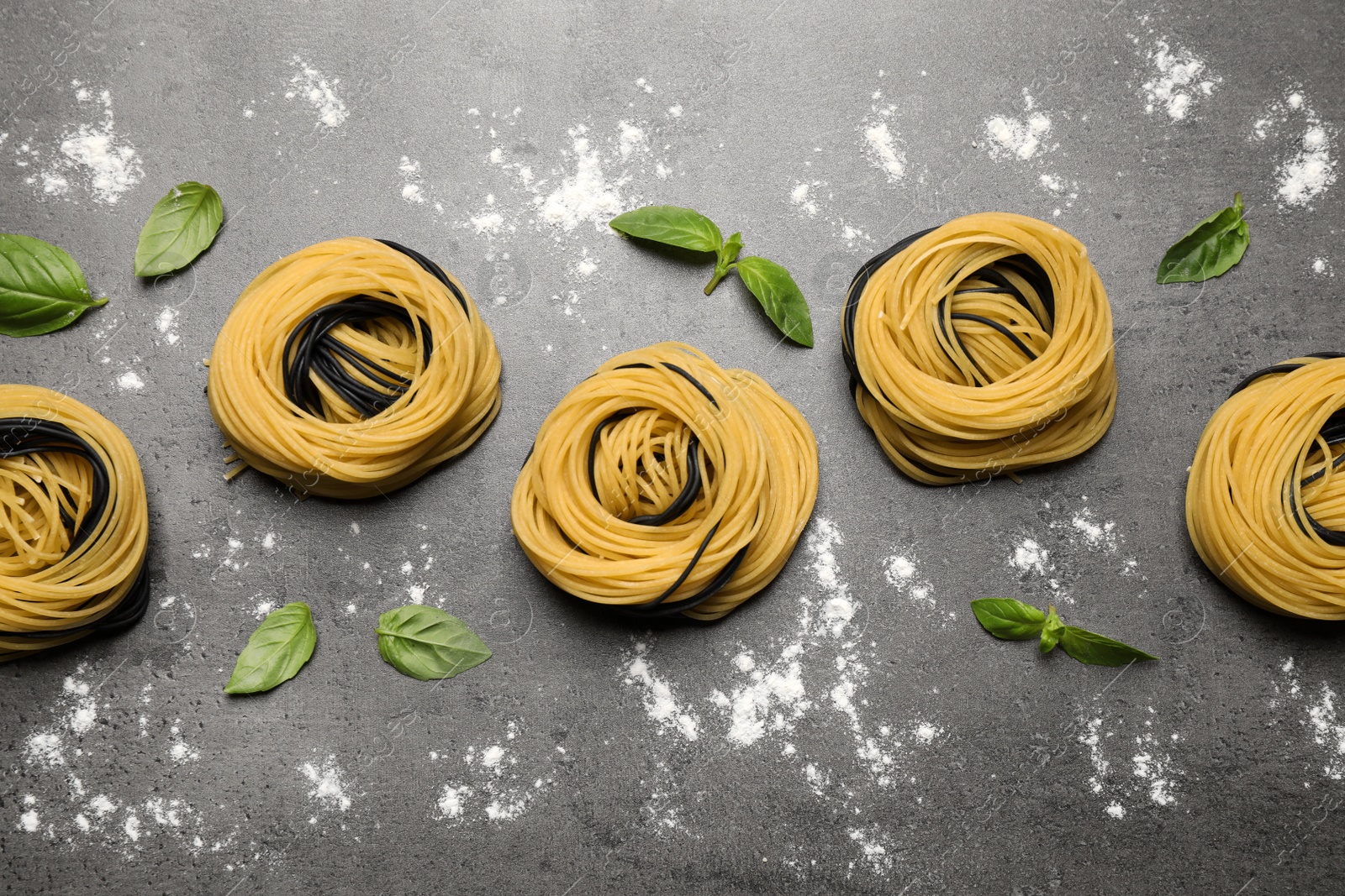 Photo of Raw linguine pasta with basil on grey table, flat lay