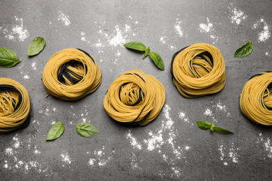 Raw linguine pasta with basil on grey table, flat lay